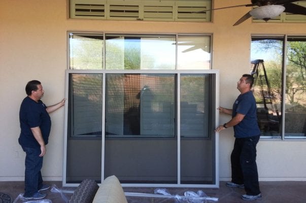 Two men are working on a sliding glass door.